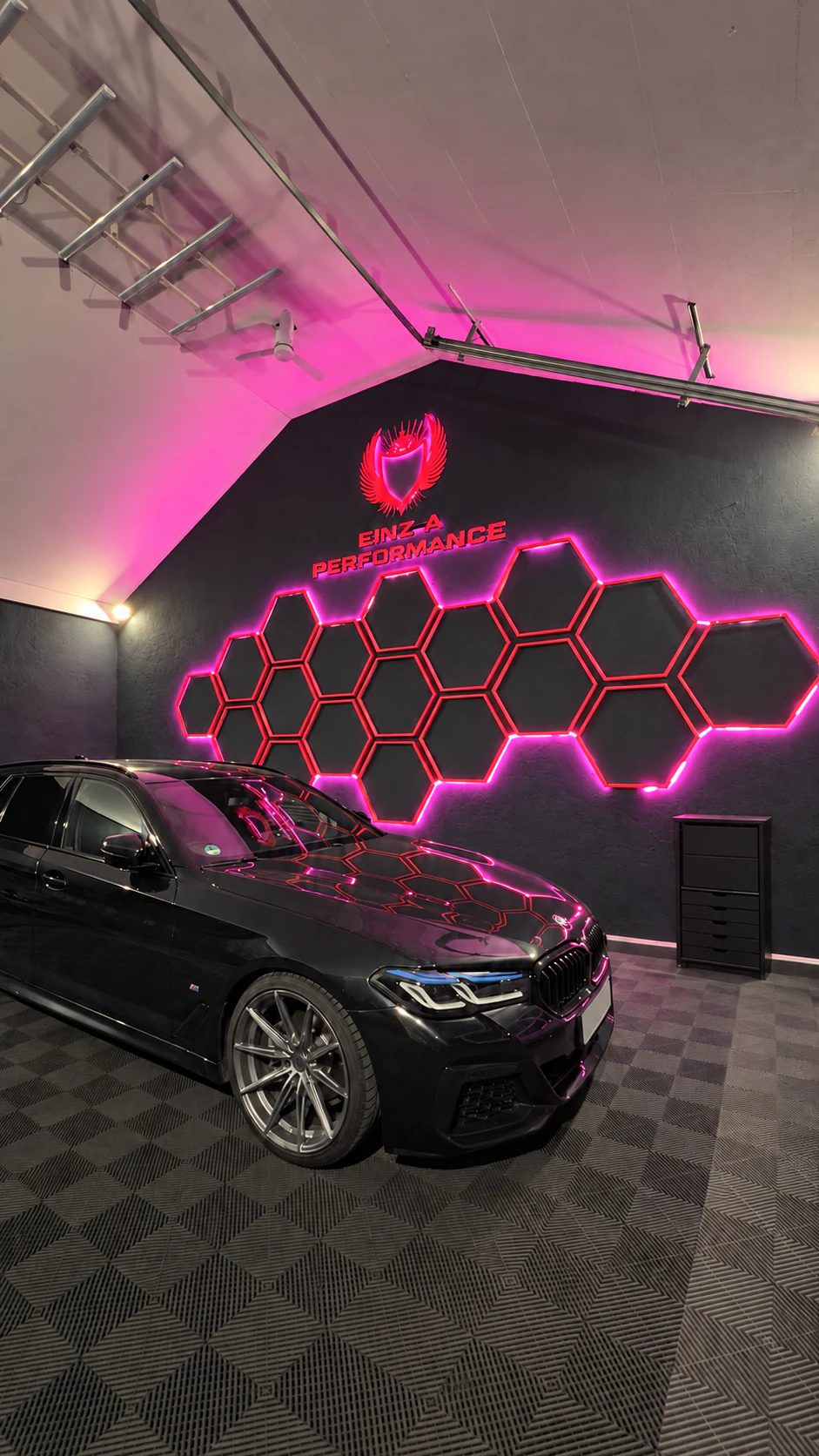 Fahrzeugwerkstatt von Einz A Performance mit schwarzem BMW und beleuchteter Logowand